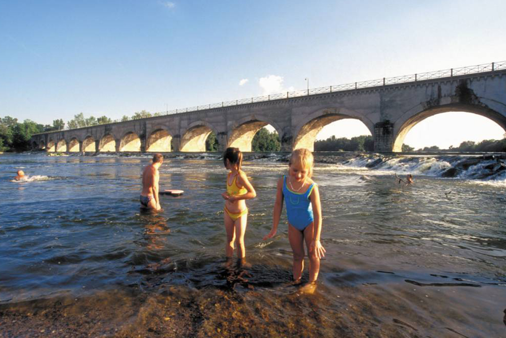 A family swimming break on a beach at the foot of the Guétin Bridge-Canal